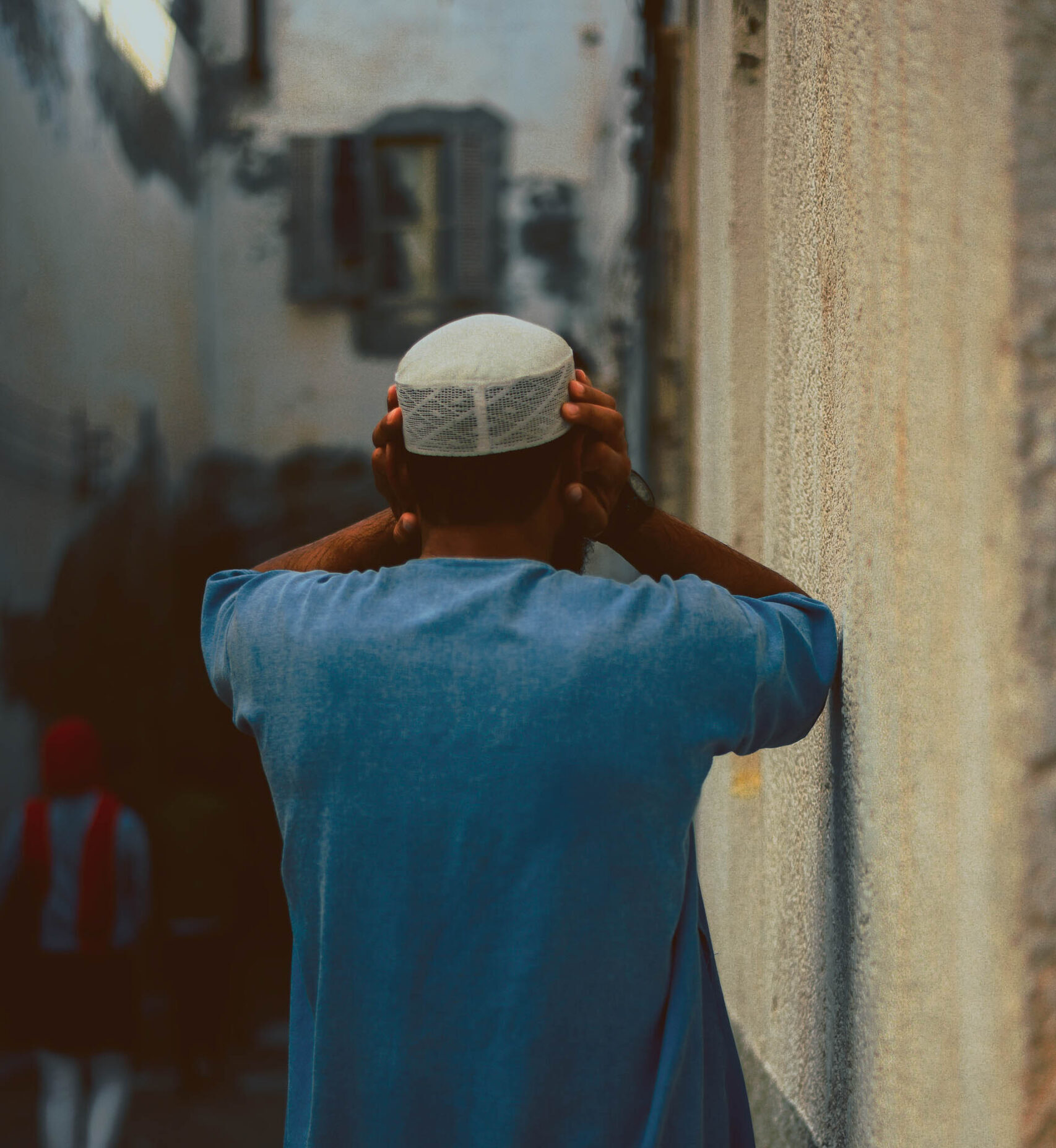 A Libyan male cover his ears wearing a white hat and blue shirt