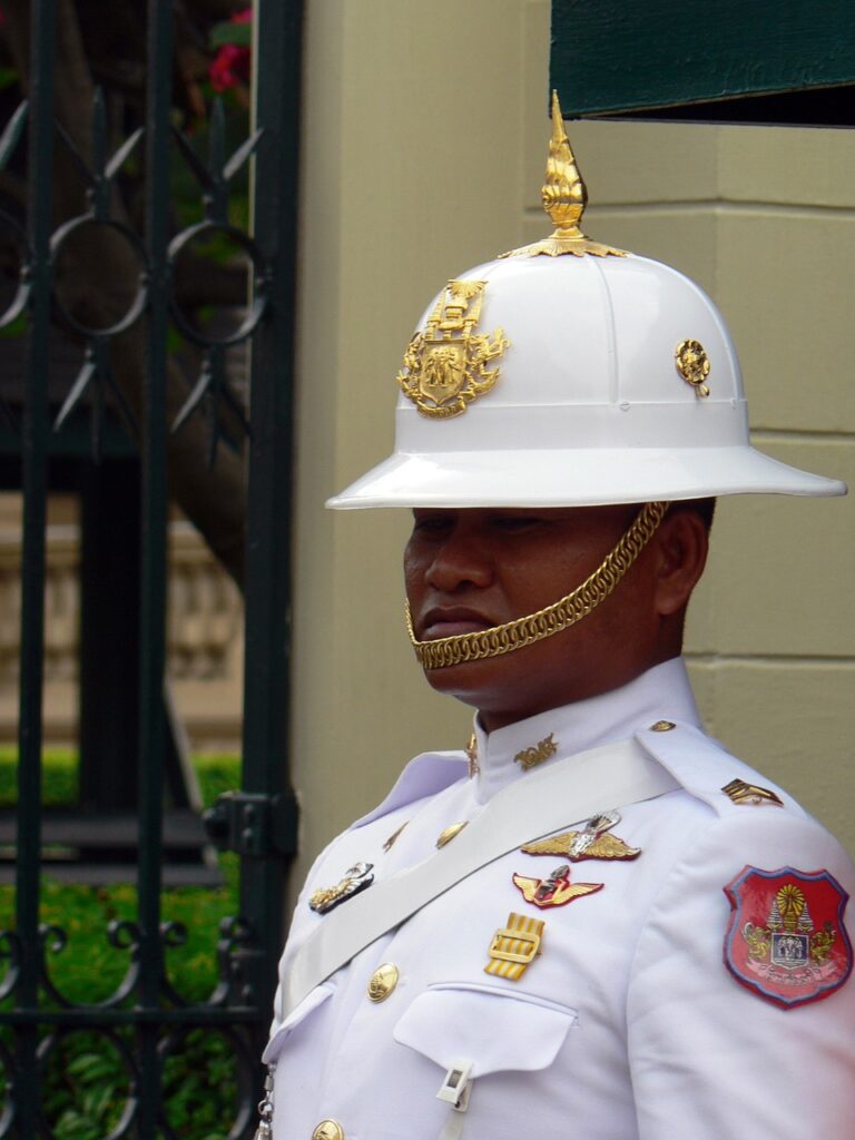 A Thai Royal guard in white with gold details stands starring with a serious look