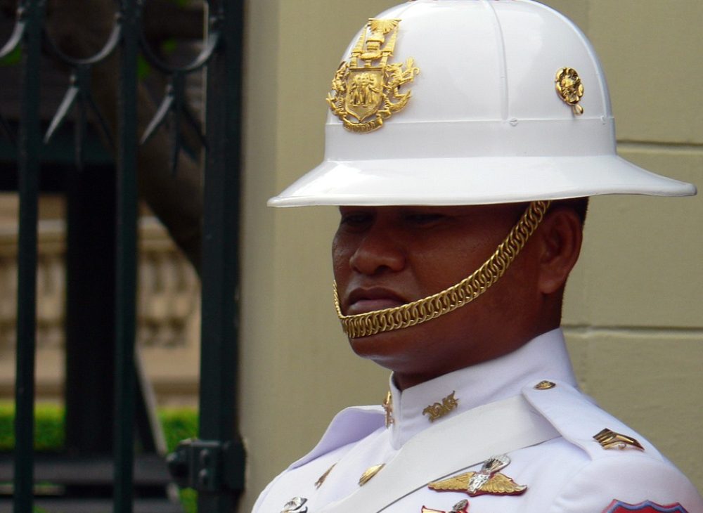 A Thai Royal guard in white with gold details stands starring with a serious look